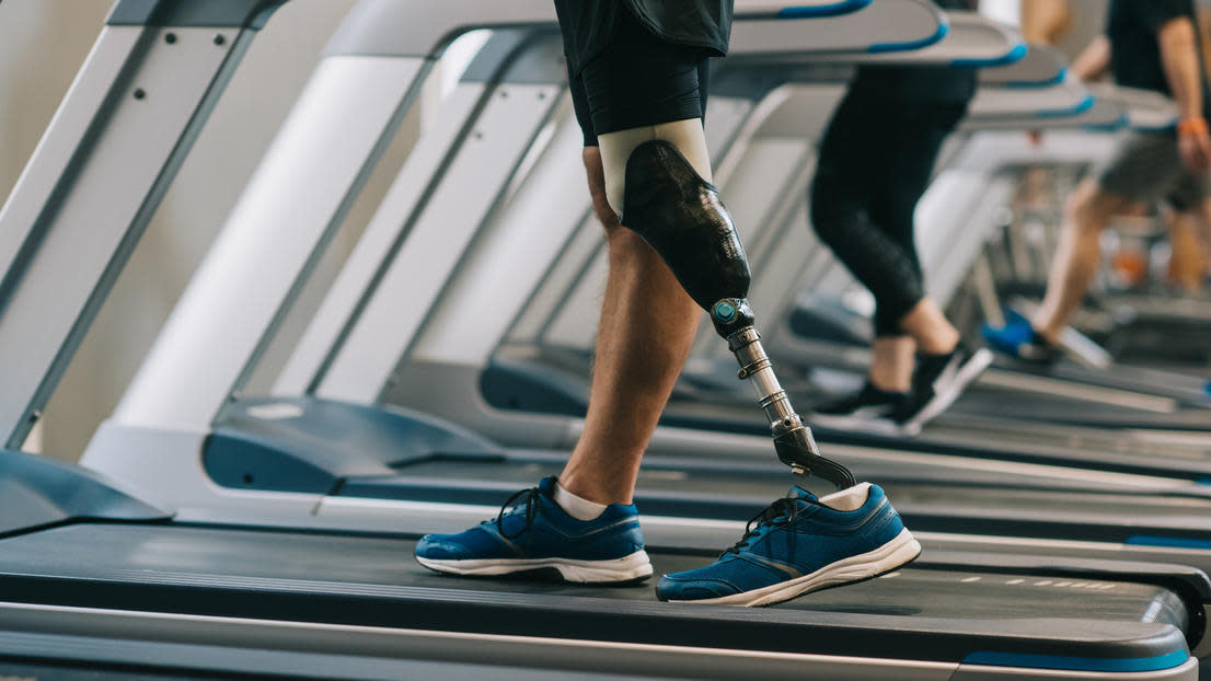 Cropped shot of man with artificial leg walking on treadmills at gym with other people
