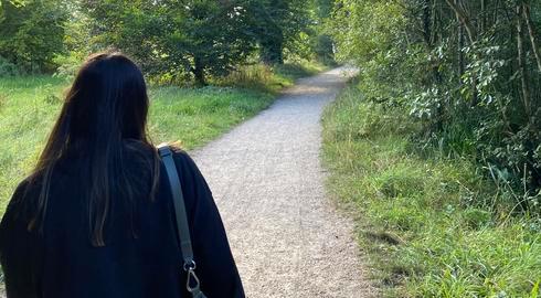 Arisha Atif walks down a smooth and winding gravel pathway between verdant trees and grass