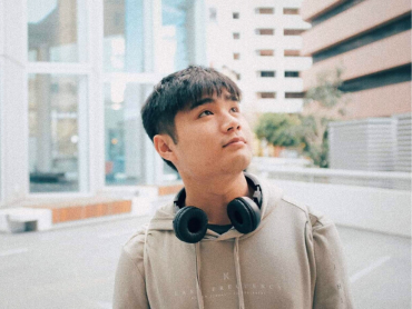 Kenton looks upwards while wearing a hoodie and over-ear headphones in a small car park