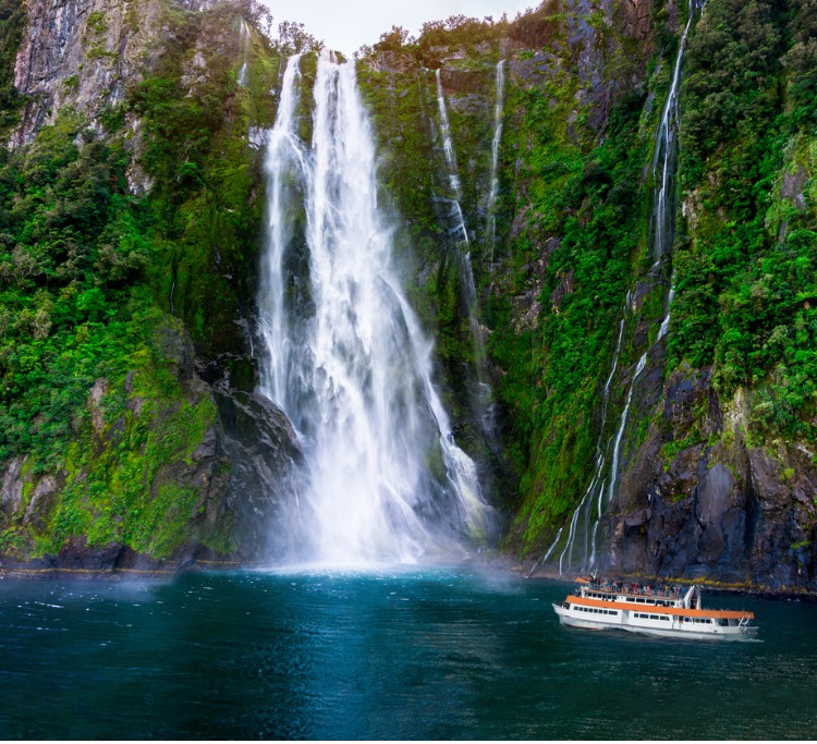 Stirling Falls at Milford Sound in South Island of New Zealand. Tourist ferry approaching Stirling Falls, the greatest waterfalls in Milford Sound, New Zealand.