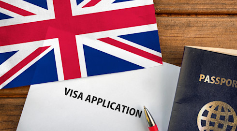 A visa application form rests on a wooden table alongside a pen, passport, and UK flag