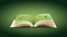 Illustration of a book open on two pages that form a football pitch. Eleven dummy players stand on it, with a football ahead of them.