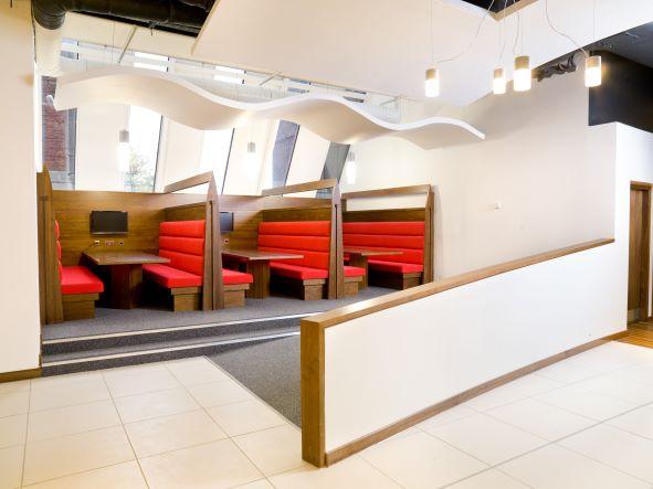 Three group study pods containing adjacent soft bench seating, a screen and a table each at the University of Glasgow. The pods are accessed by two small steps or a ramp.