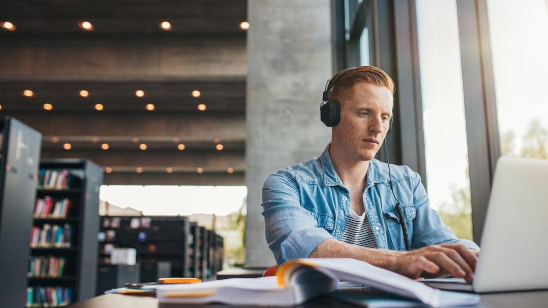 Young male student with headphones studying on the laptop