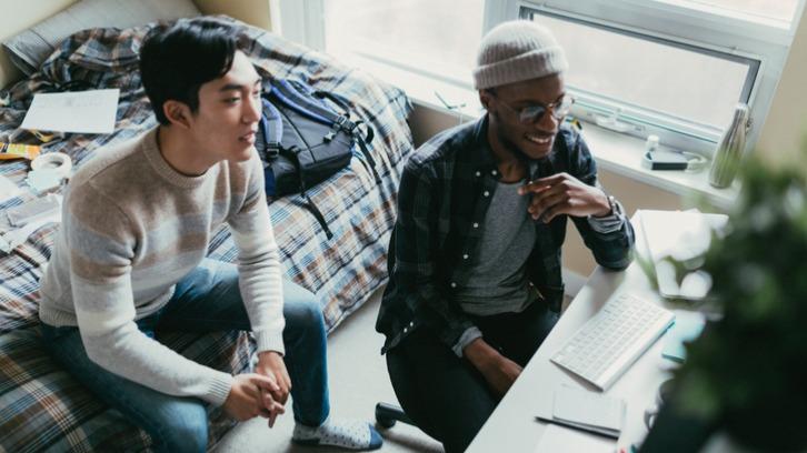 Two friends watching something on a laptop in a bedroom