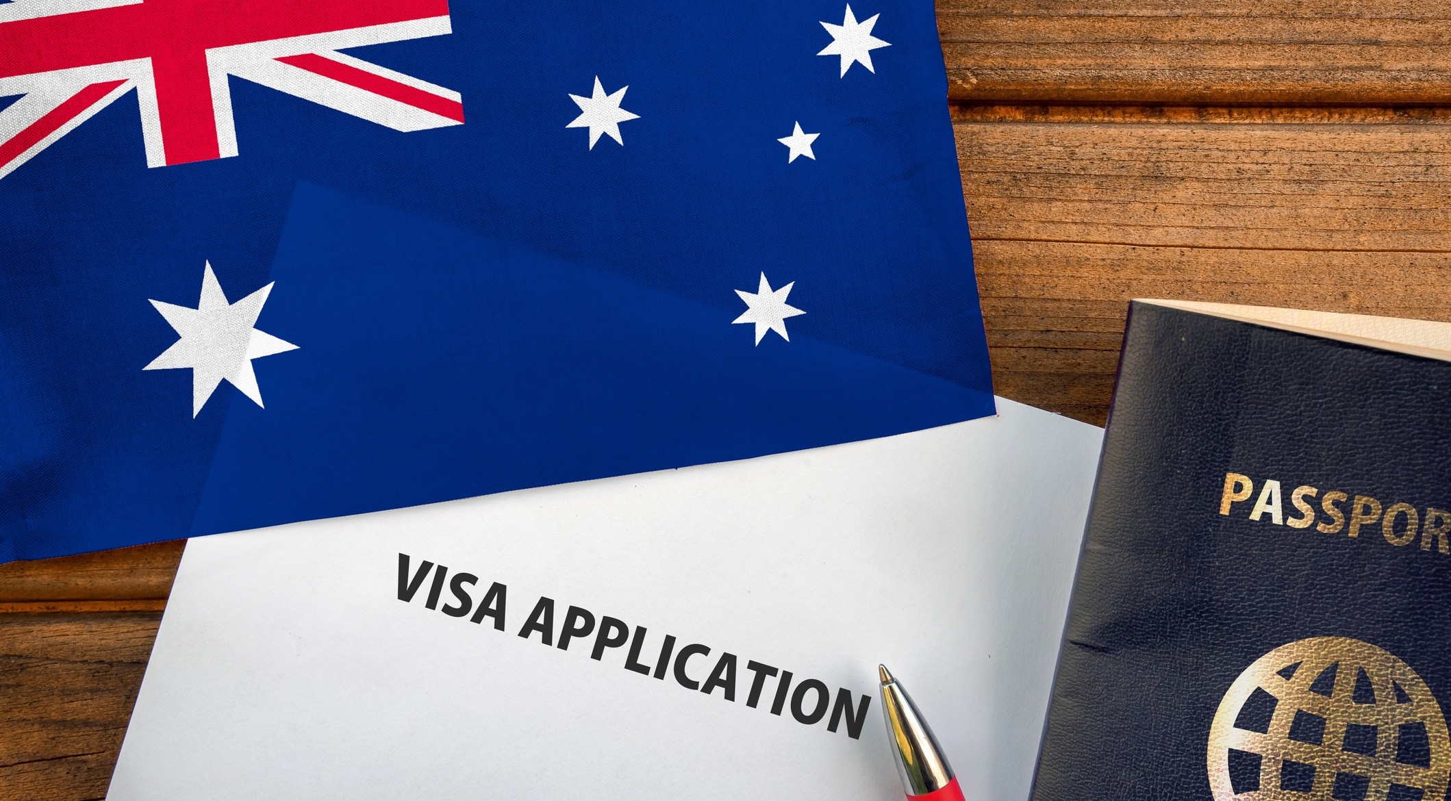 A pen, passport, flag of Australia and visa application document are placed on a wooden table