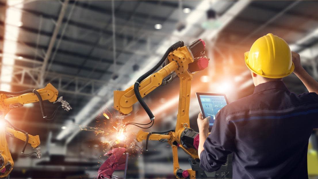 Engineer using tablet to check and control automation robot arms machine.