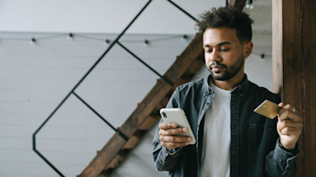 Man standing up while on his phone and holding his eftpos card 