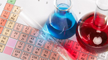 Periodic table underneath a test tube and jars with blue and red liquids