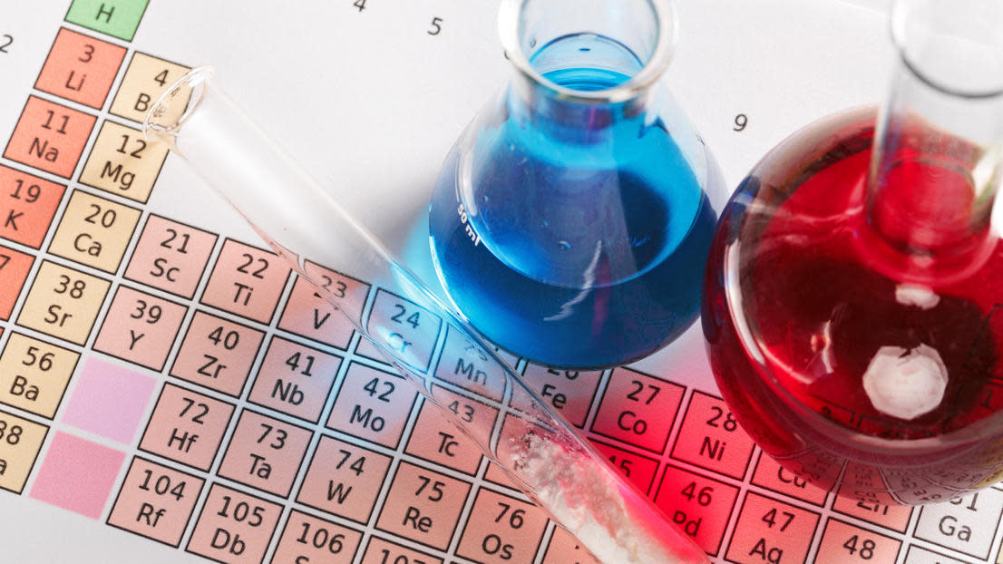 Periodic table underneath a test tube and jars with blue and red liquids