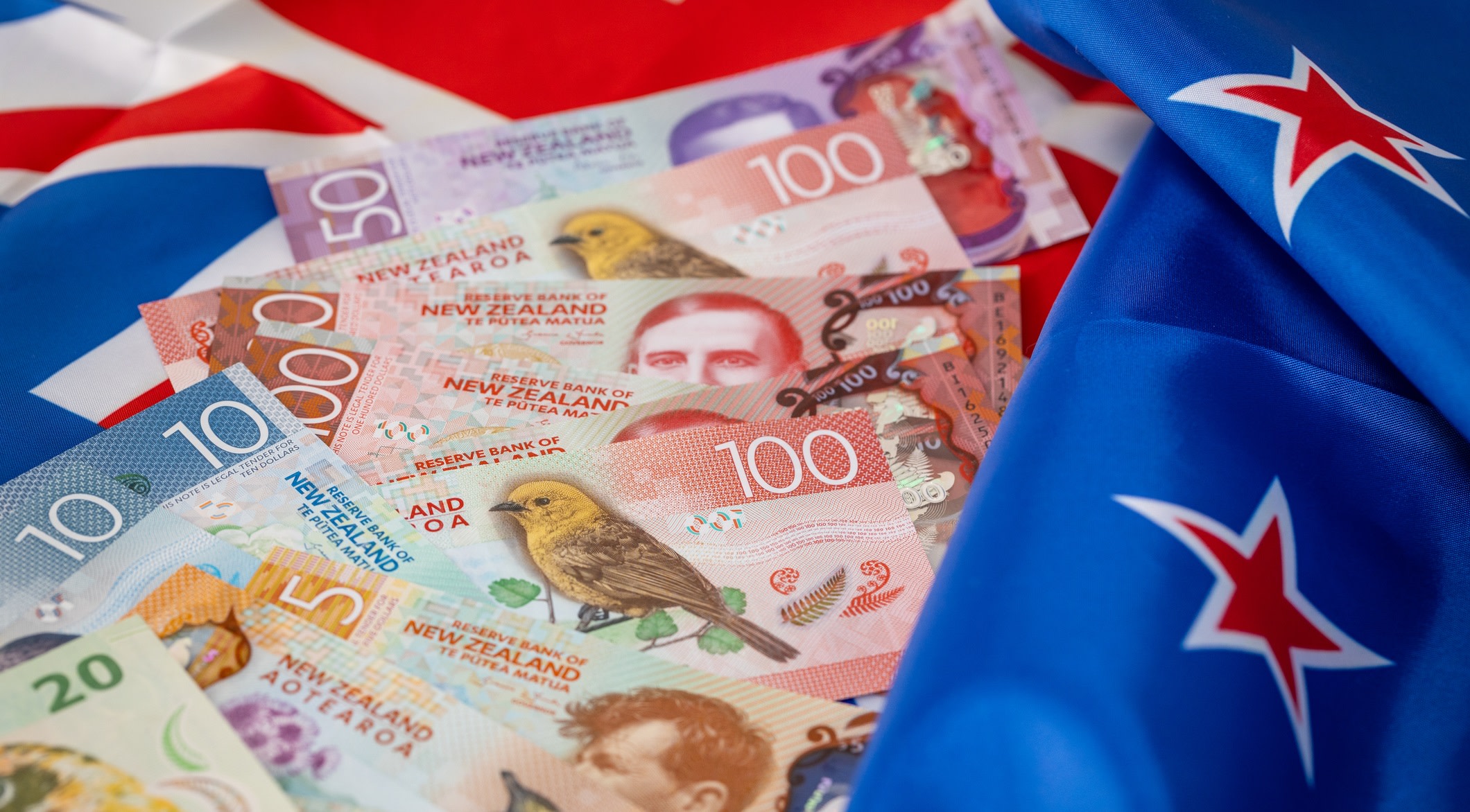 Numerous New Zealand banknotes rest on top of the country's flag