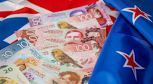 Numerous New Zealand banknotes rest on top of the country's flag