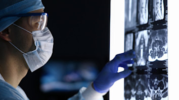 Doctor in surgical clothes and mask looking at vertebral MRI scan