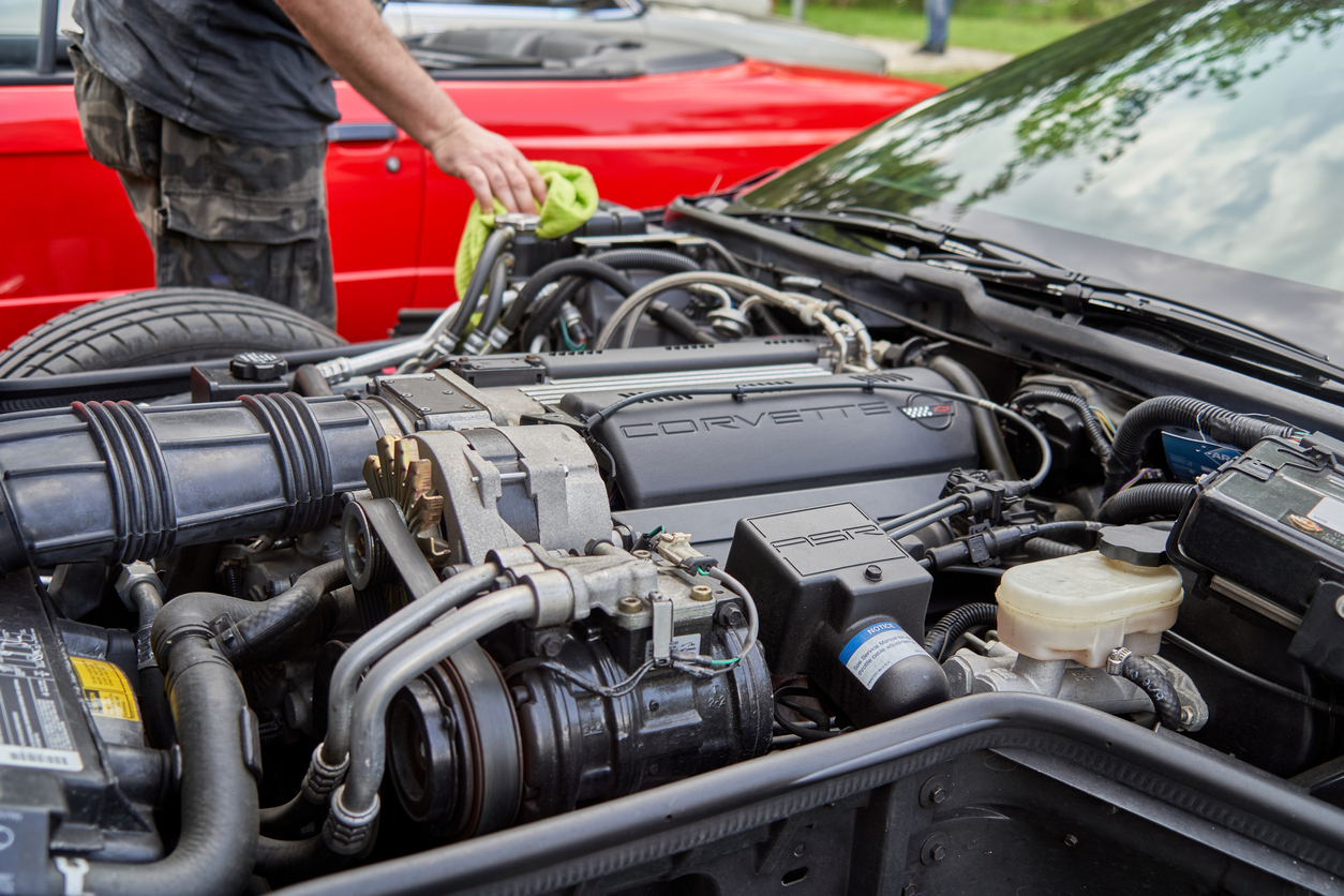 A man carefully cleans the engine of a Chevrolet Corvette using a linen cloth
