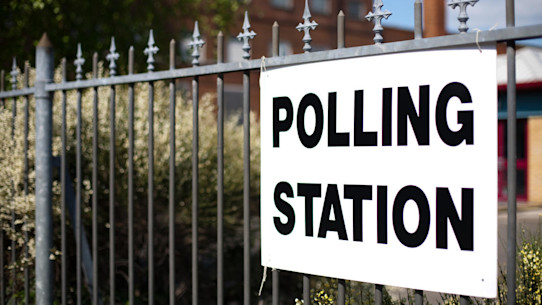 Metal fence with white cardboard sign saying 'polling station' in black capital letters