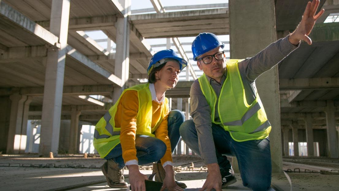 Two architects kneeling on the floor and discussing over blueprint