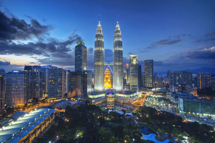 The Petronas Towers in Kuala Lumpur, lit up at dusk. Many other tall buildings stand beside them.