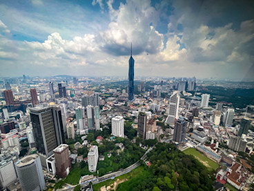 The Kuala Lumpur skyline, with many tall buildings, including the tallest, Merdeka 118, separating parkland in the foreground from mountains in the far distance