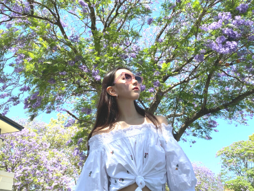 Jennifer looks upwards through sunglasses as she stands in front of a blossom tree