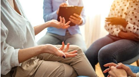 A psychologist takes notes while patients talk to each other.