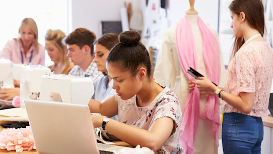 Several students working on laptops and with textiles