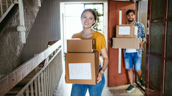 Curly-haired girl in a yellow jumper packing books into moving out boxes