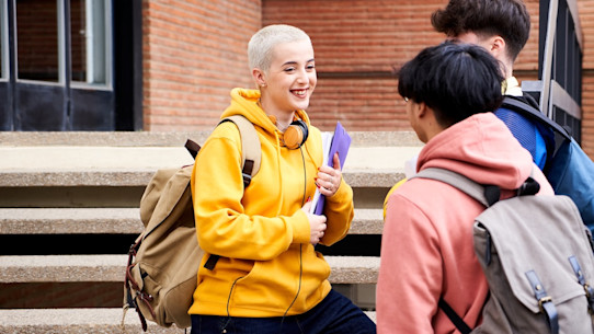 Three students smiling and talking to each other at the university entrance