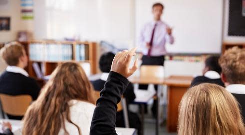 A school student raising her hand to ask the teacher a question in a classroom.