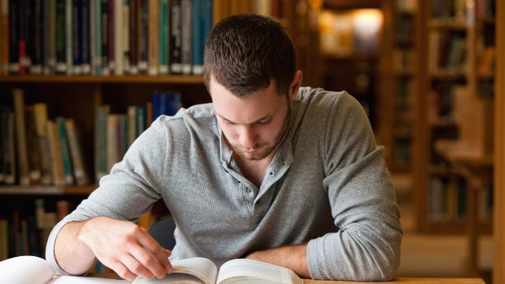 Male student researching with a book in a library