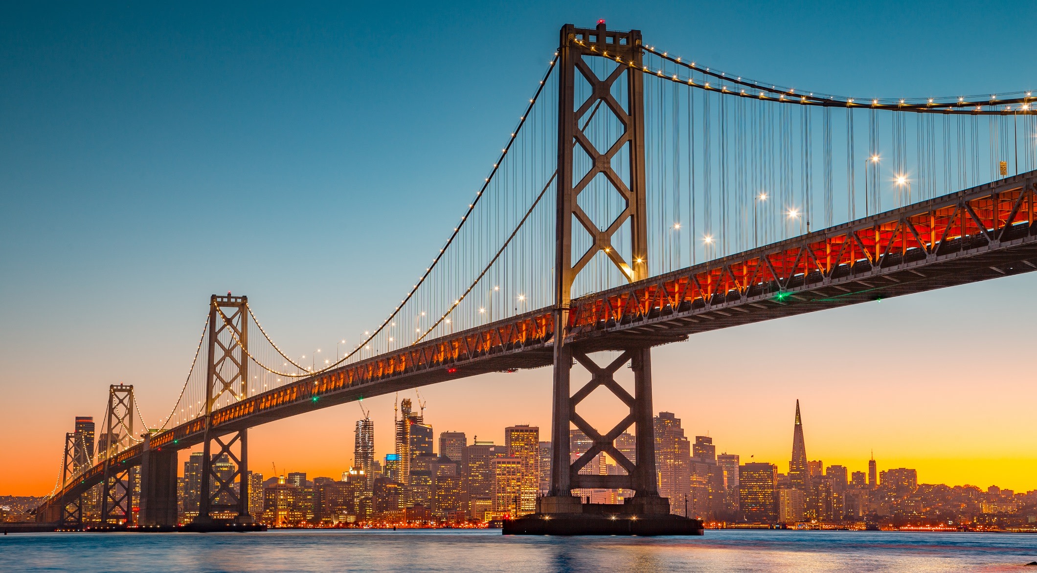 The side of Oakland Bay Bridge at dusk, viewed from San Francisco Bay towards the city
