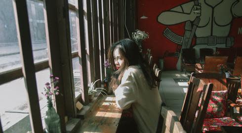 A woman sits at a coffee shop counter looking out of the window. 