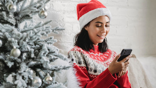 Woman receiving gift on phone wearing a Christmas hat