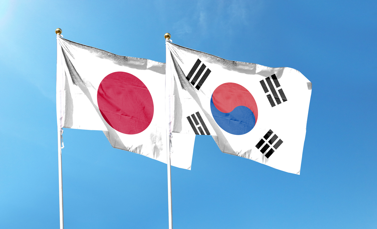 The flags of Japan and South Korea stand next to each other before a blue sky