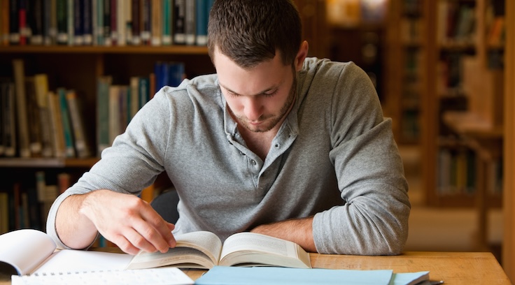 Male student researching with a book