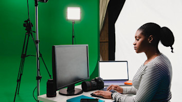 Cinematics student on computer with equipment by green screen