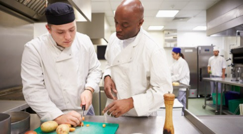 A chef teaching a chef student how to cut vegetables.