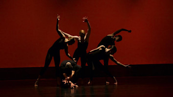 People on stage with red backdrop and dark lighting