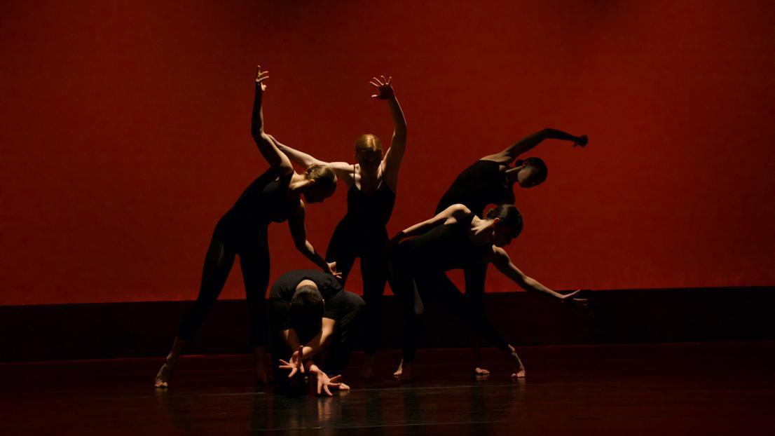 People on stage with red backdrop and dark lighting
