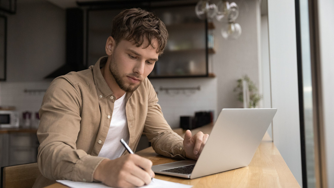 A student looking at a laptop and writing notes