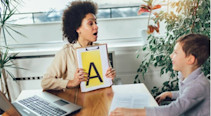 A speech therapist working with a child, holding up a sign with the letter 'A' on it.