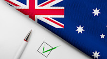 Graphic featuring a green checkmark and a pen on a white background, all of which is down to the left of a section of the Australian flag