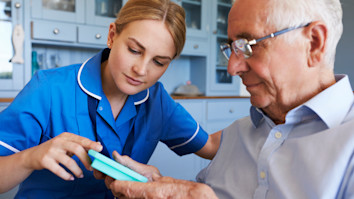 Nurse helping an old man to organise medication on home visit