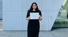 Advayta Zadoo stands in front of a concrete building while holding her Advantage Award certificate from University College Dublin