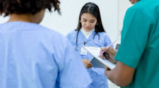Group of three medical students in scrubs taking notes in clinical setting.