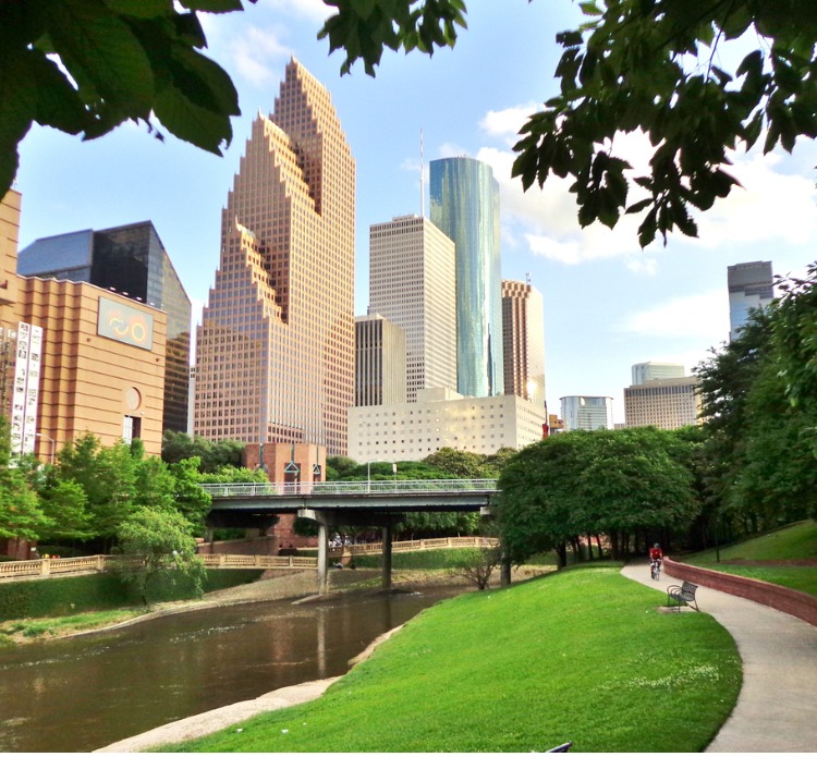 Wide shot of Houston's modern skyline and paved bicycle/walking path in Buffalo Bayou Park on a summer afternoon