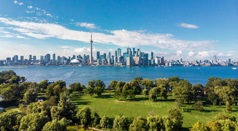 Lake Ontario separates verdant, tree-lined parkland from the wide Toronto skyline ahead of it, within which the CN Tower reaches highest into the blue sky