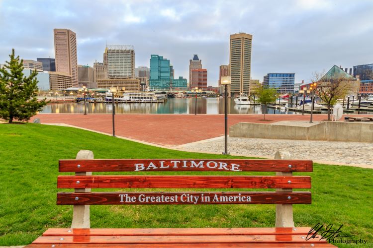 Baltimore city in the background. Park bench in the foreground with the words Baltimore The Greatest City in America