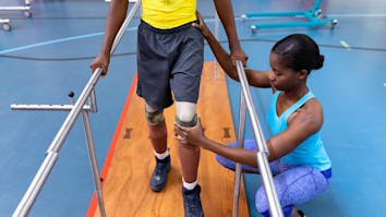 Physiotherapist assisting disabled man walk with parallel bars in sports centre