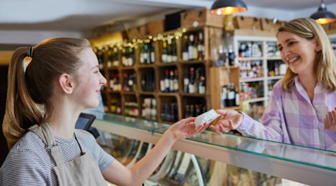 Teenage girl serving a woman at delicatessen counter