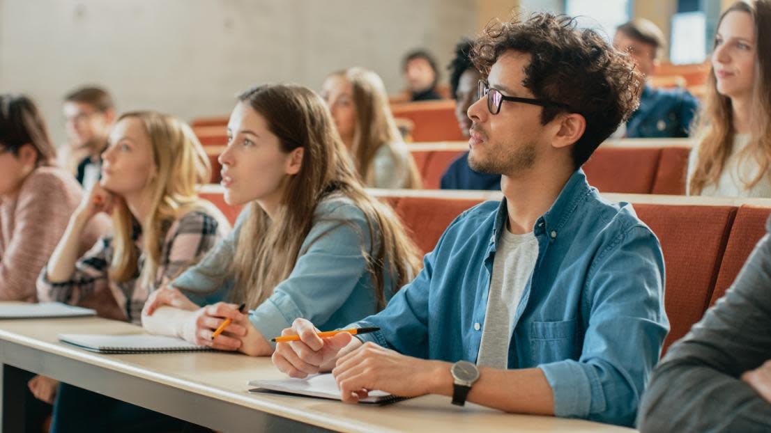 Students Listening to a Lecturer and Writing in Notebooks